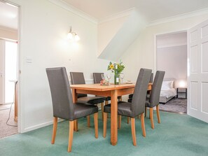 Un coin repas avec une table en bois et six chaises, un vase rempli de fleurs et un luminaire fixé au mur.