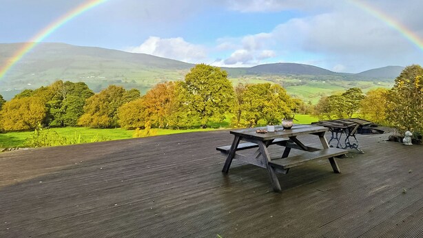 A wooden deck with picnic tables overlooking a valley with a rainbow. - 2 bedroom accommodation in Penybntfawr, near Oswestry (Penybntfawr, near Oswestry)