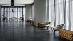 A spacious room with a dark tiled floor, large windows with sheer curtains, and a mix of modern and classic furniture including tufted sofas and wicker chairs.