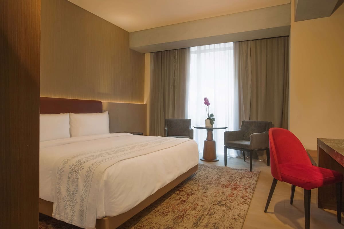 A hotel room with a large bed, a desk, two chairs, and a small table with a plant.