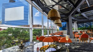 An outdoor dining area with a view of a modern building, tables with chairs, and a hanging light fixture.