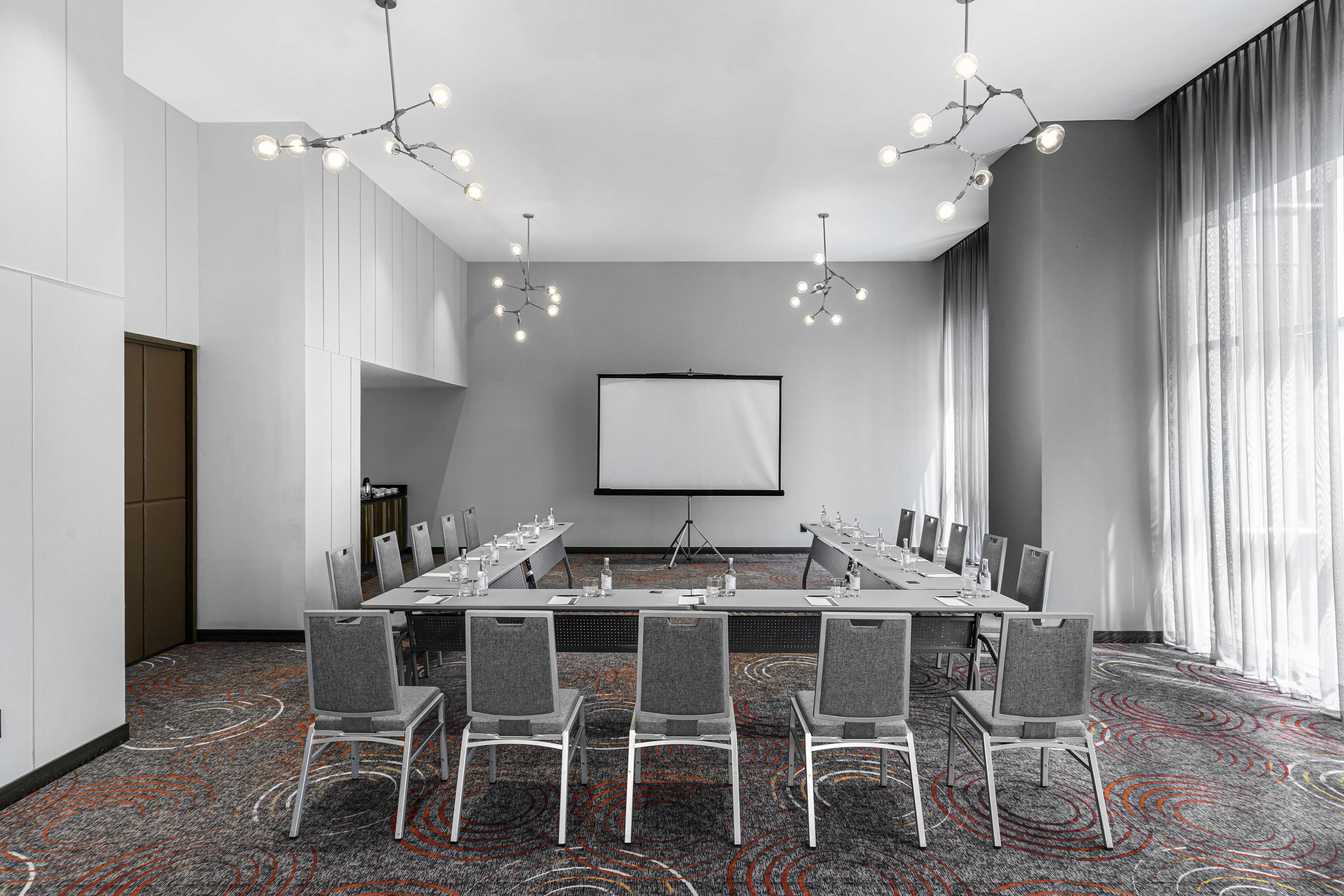 A conference room with a long table, chairs, a projector screen, and a carpeted floor.