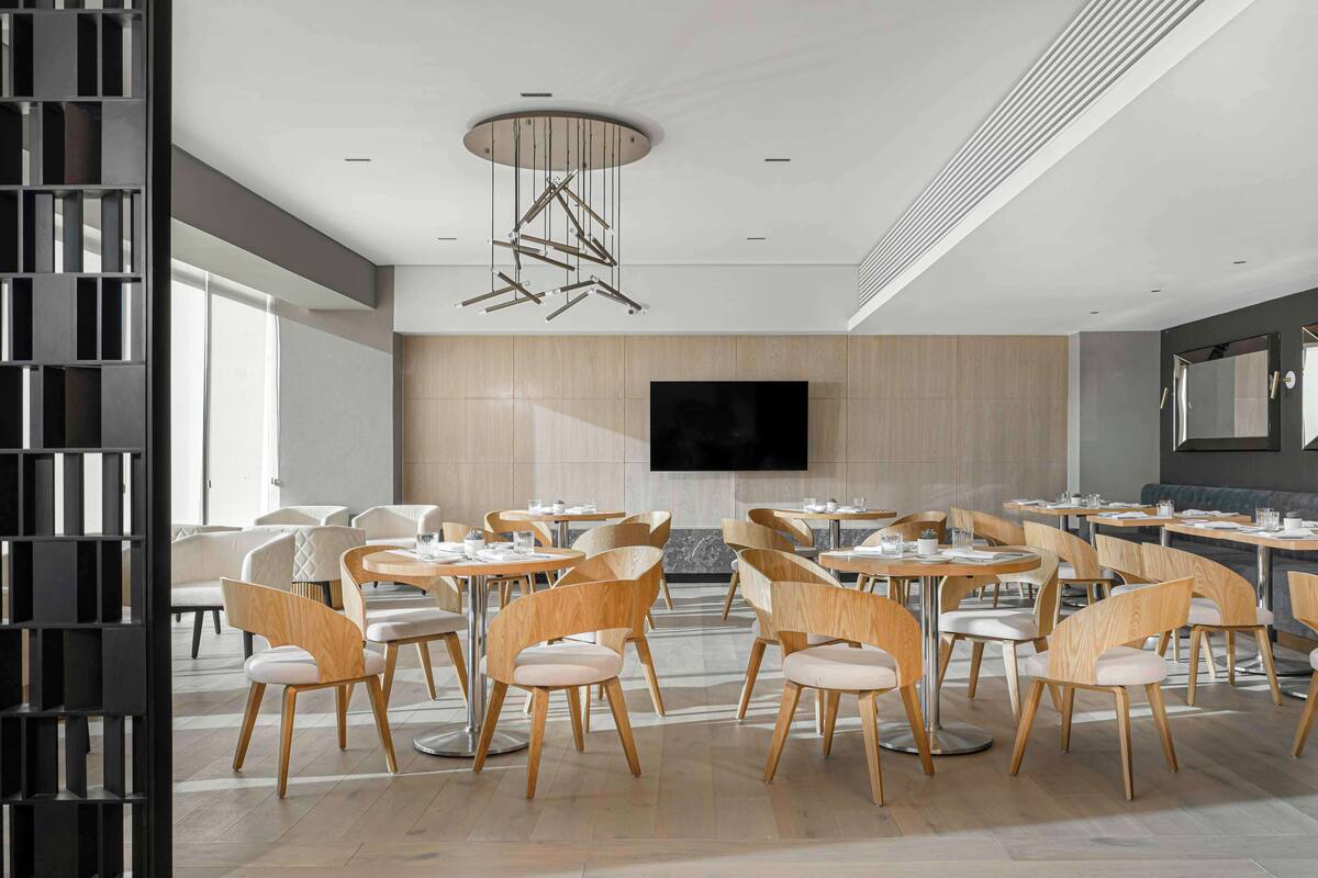 A modern dining area with round tables and wooden chairs, a large flat-screen TV on the wall, and a contemporary ceiling light fixture.