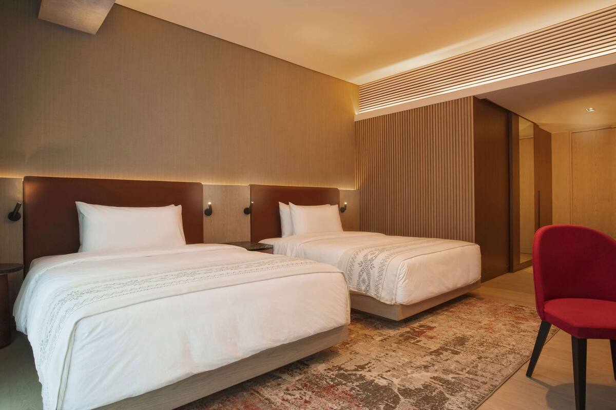 A hotel room with two beds, a red chair, and a modern design.