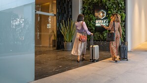 A modern hotel lobby with a glass entrance, a potted plant, and a sign for the Hyatt Regency.