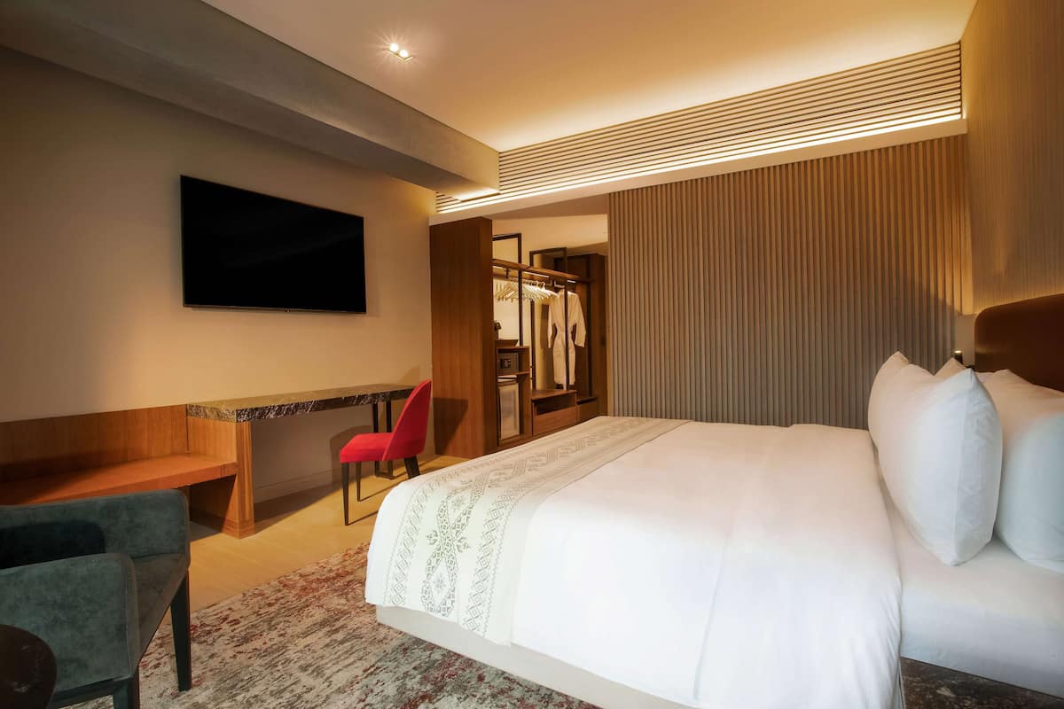 A hotel room with a large bed, a desk, a chair, a TV, and a wardrobe.