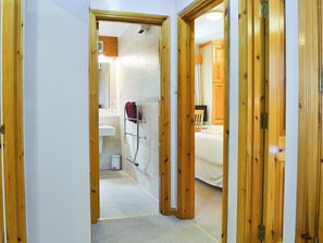 Un corridoio che porta al bagno, dove si trovano una doccia, un lavandino e un water.