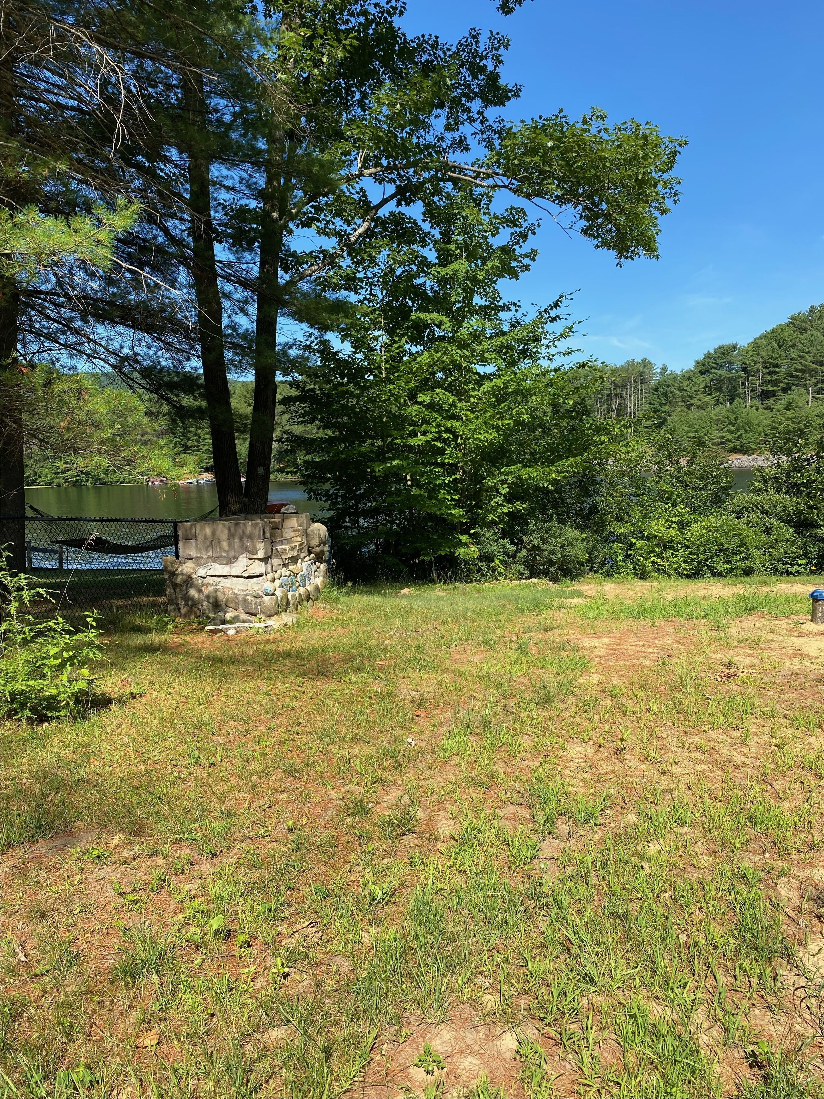 A natural outdoor area with a stone structure, a grassy field, and a body of water in the background.
