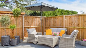 Eine Terrasse mit Korbmöbeln, einem Holzzaun und Kübelpflanzen.