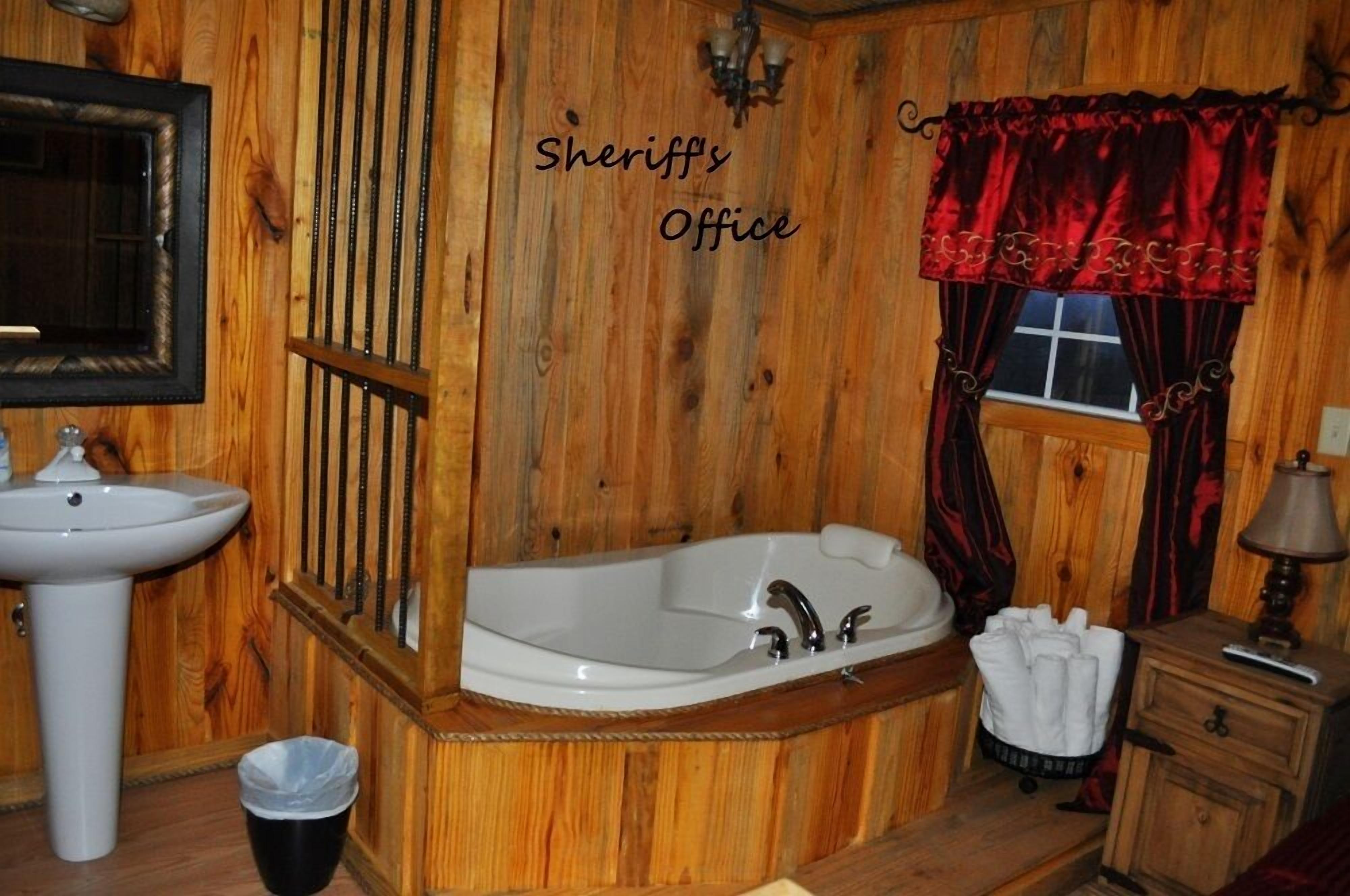 Un baño de madera con lavamanos, bañera y ventana con cortinas rojas.