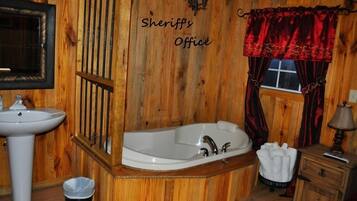 Un baño de madera con lavamanos, bañera y ventana con cortinas rojas.