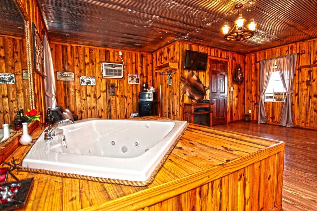 A wooden cabin interior with a large bathtub, wooden walls, a chandelier, and various signs.