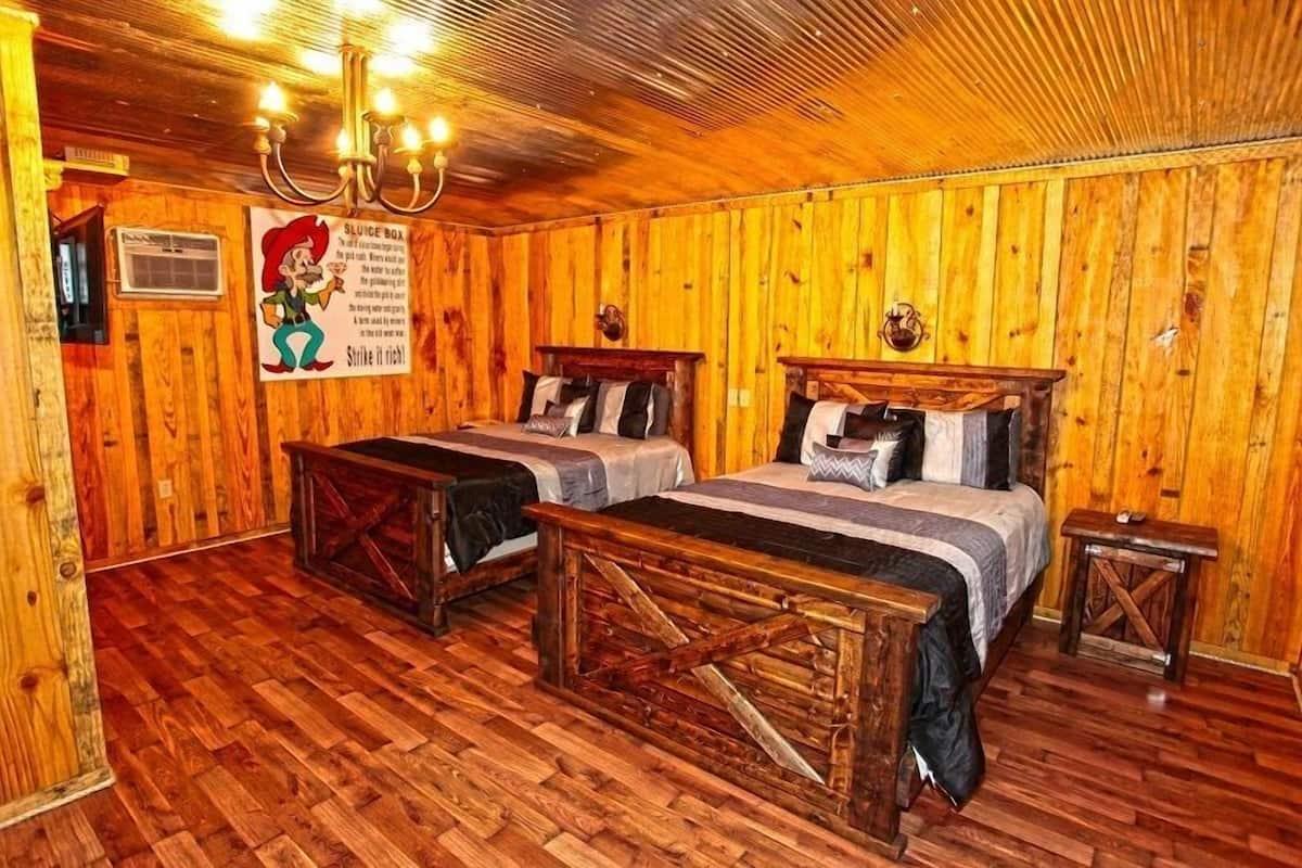 A rustic wooden room with two beds, a bench, and a chandelier.