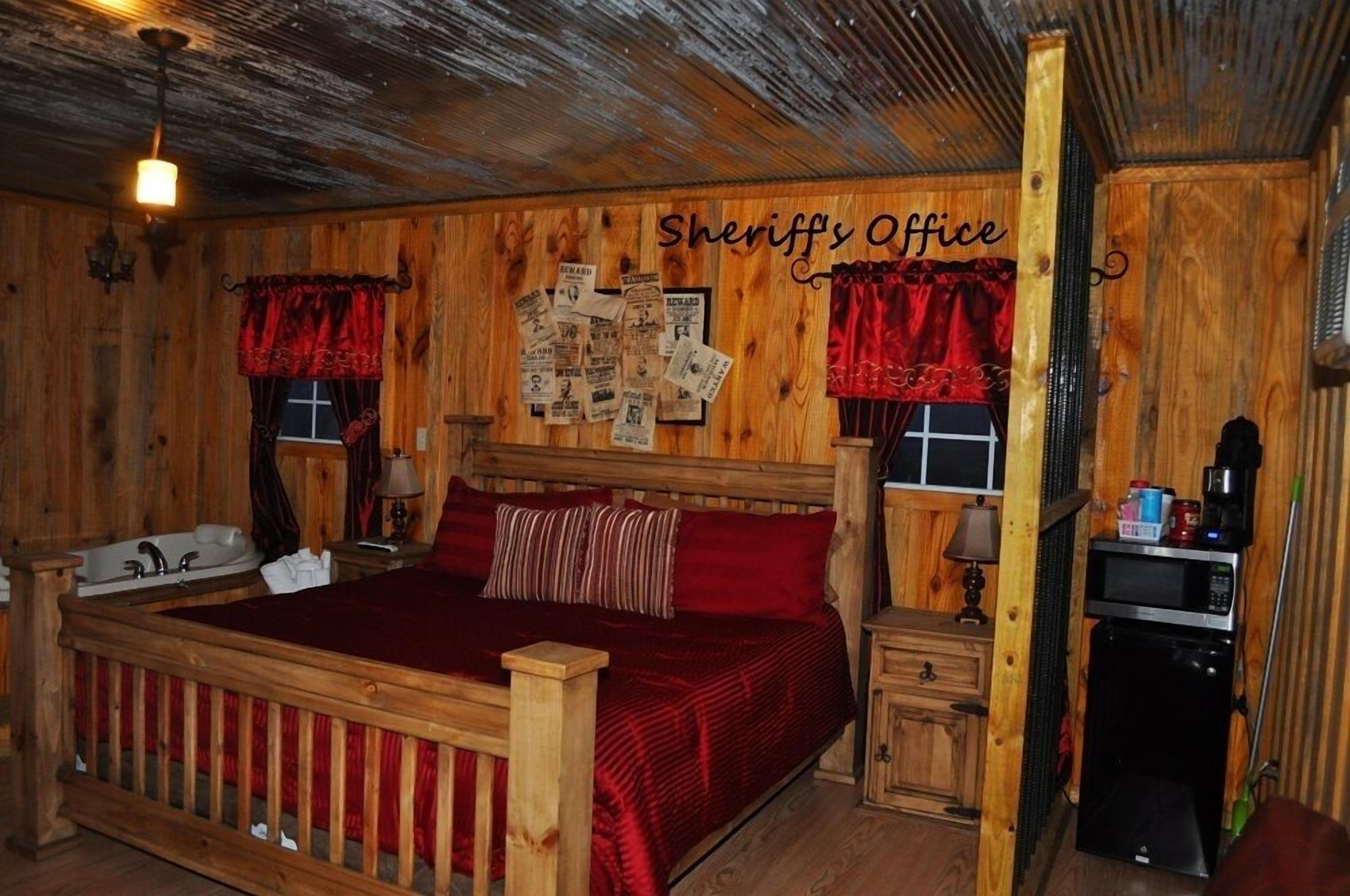 A wooden room with a bed, a small desk, a sink, and a microwave.