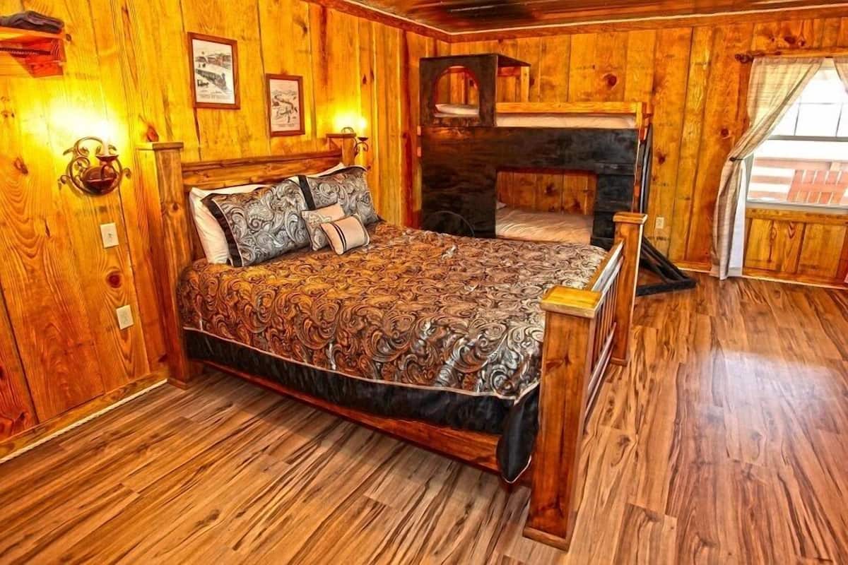 A wooden-paneled bedroom with a large bed, a fireplace, and framed pictures on the walls.