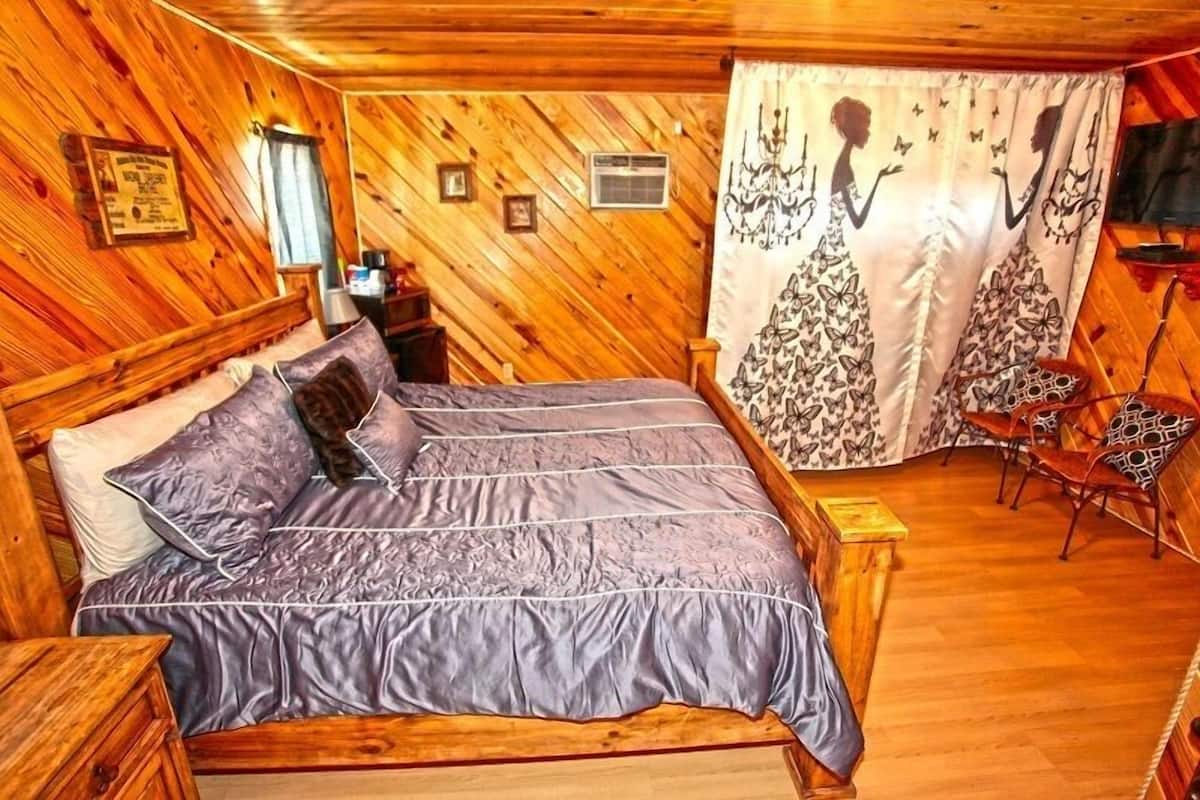 A wooden-paneled bedroom with a bed, a nightstand, a chair, and a curtain with a butterfly design.
