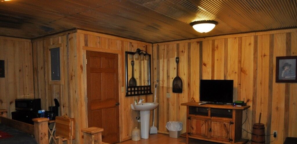 Une pièce aux murs lambrissés, avec une porte en bois, un évier, une télévision et un meuble.