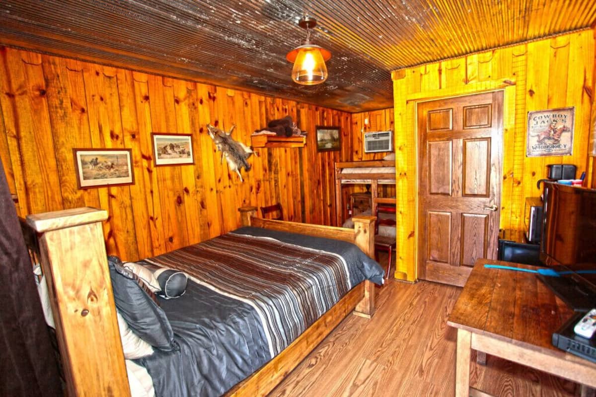 A rustic wooden room with a bed, a desk, and a door.
