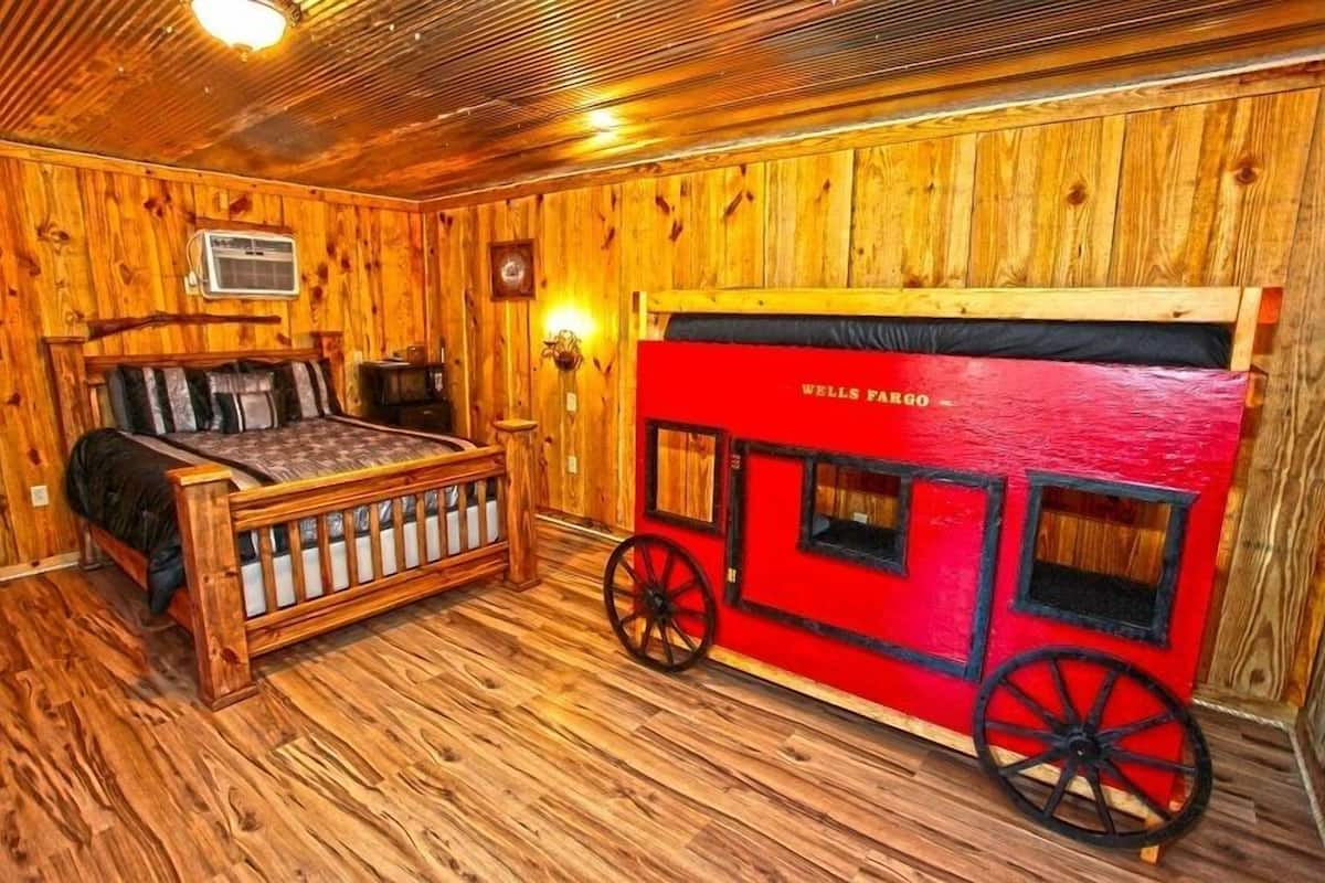 A wooden room with a bed, a red wagon, and a clock on the wall.