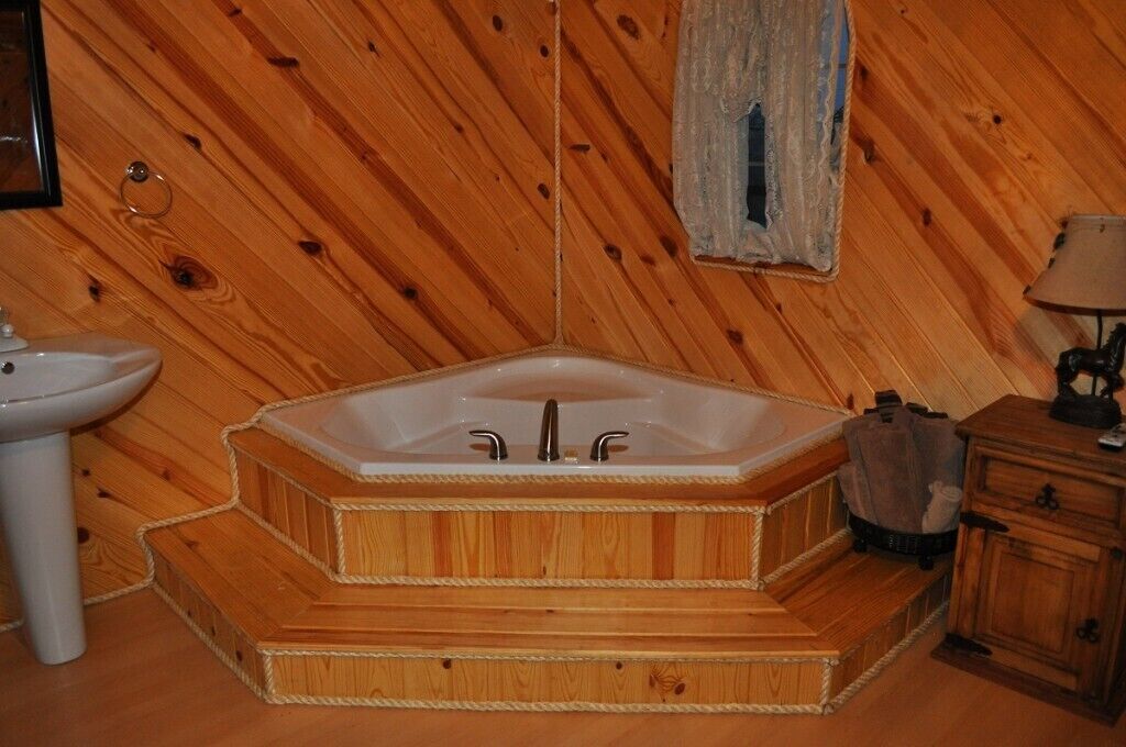 Baño de cabaña de madera con una bañera de madera, un lavabo y un armario.