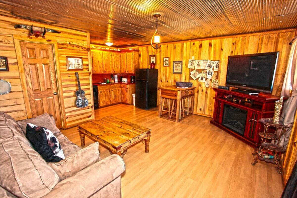 A cozy wooden cabin interior with a sofa, coffee table, TV, and a fireplace.