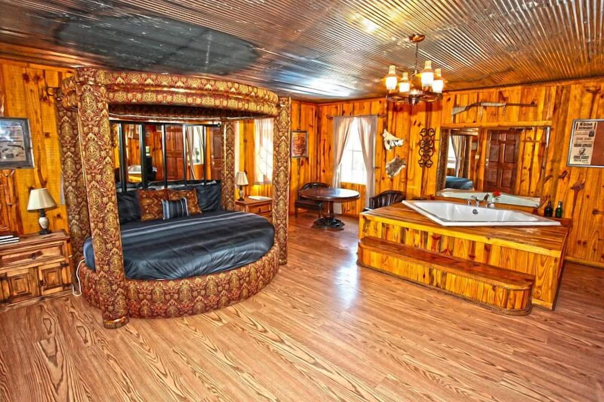 A log cabin-style room with a four-poster bed, a wooden bench, a sink, and a mirror.