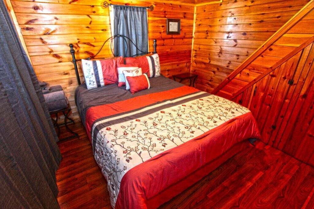 A wooden cabin bedroom with a bed, a chair, and a staircase.
