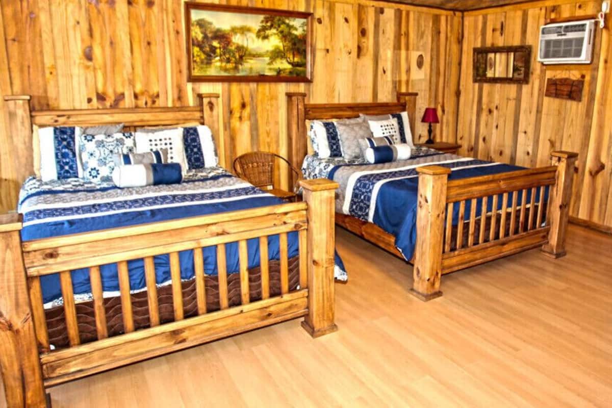 A wooden room with two beds, a chair, and a painting on the wall.