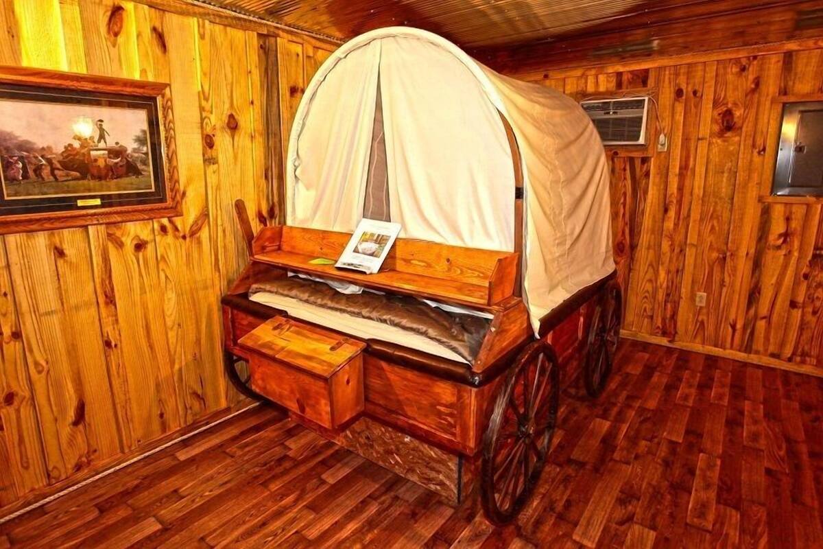 A rustic room with a wooden floor, a bed with a canopy, a framed picture on the wall, and a small table with a magazine.