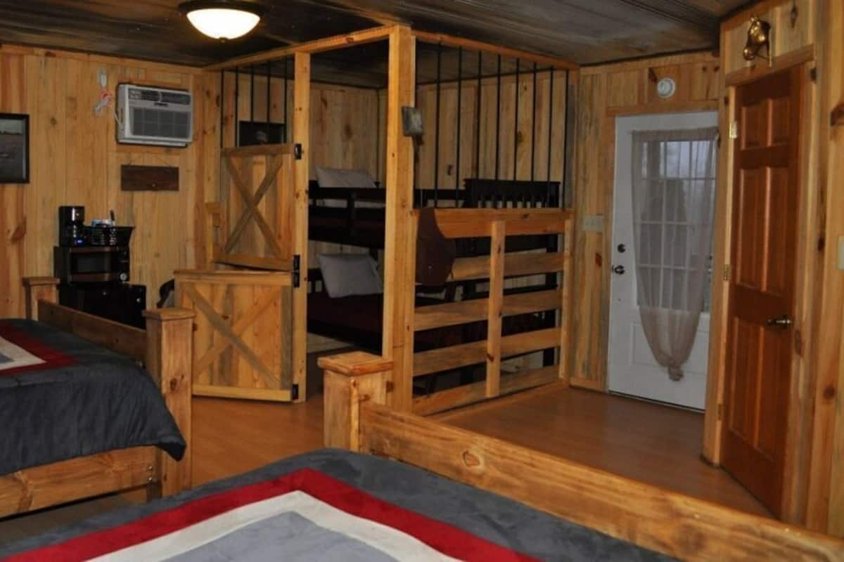 A wooden cabin-style room with bunk beds, a desk, and a door.