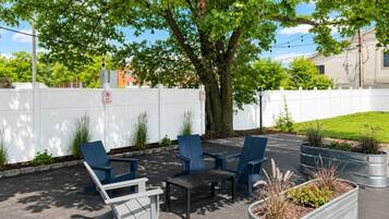 An outdoor seating area with chairs and tables, a tree, and a white fence.