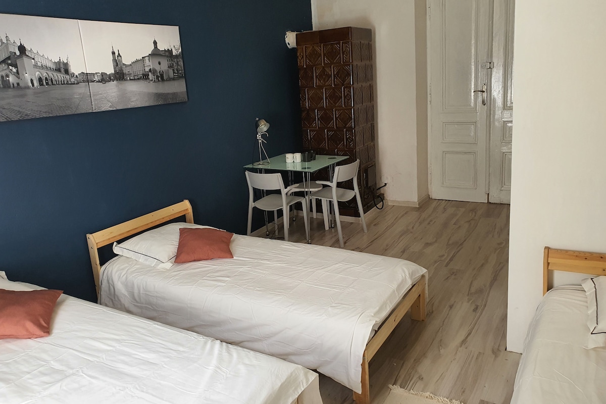 A room with two beds, a desk with chairs, a cabinet, and a door.