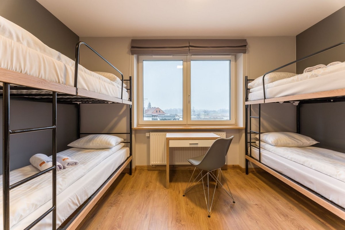Quarto em dormitório com beliches, escrivaninha e cadeira.
