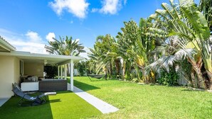 Una casa moderna con un porche cubierto, una hamaca y exuberante vegetación tropical.