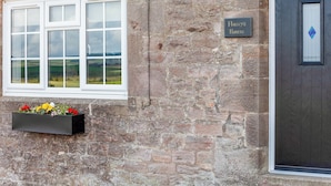 Un bâtiment en pierre avec une fenêtre blanche et une porte sur laquelle est affiché un panneau indiquant « La maison de Flossy ».