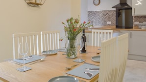 Een eetruimte met een houten tafel voor twee personen, een bloemenvaas en een keuken op de achtergrond.