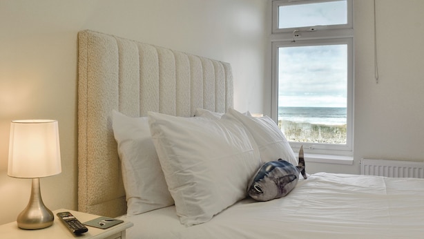 Een hotelkamer met een bed, een nachtkastje met een lamp en afstandsbediening, en een raam met uitzicht op de oceaan.
