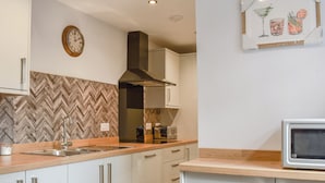 Een moderne keuken met witte kastjes, een backsplash in een herringbone-patroon, een roestvrijstalen spoelbak, een magnetron en een klok aan de muur.