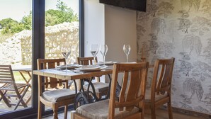 Un coin repas avec une table dressée pour quatre personnes, des chaises en bois et un téléviseur fixé au mur.