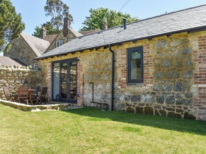 A stone building with a tiled roof, a glass door, and a small outdoor seating area with chairs. - 2 bedroom accommodation in Wroxall, near Ventnor (Wroxall, near Ventnor)