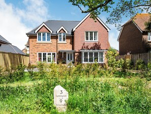 A two-story house with a brick facade, multiple windows, and a front garden.