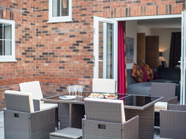 Un patio con mobiliario de mimbre, una mesa de vidrio y un muro de ladrillo.