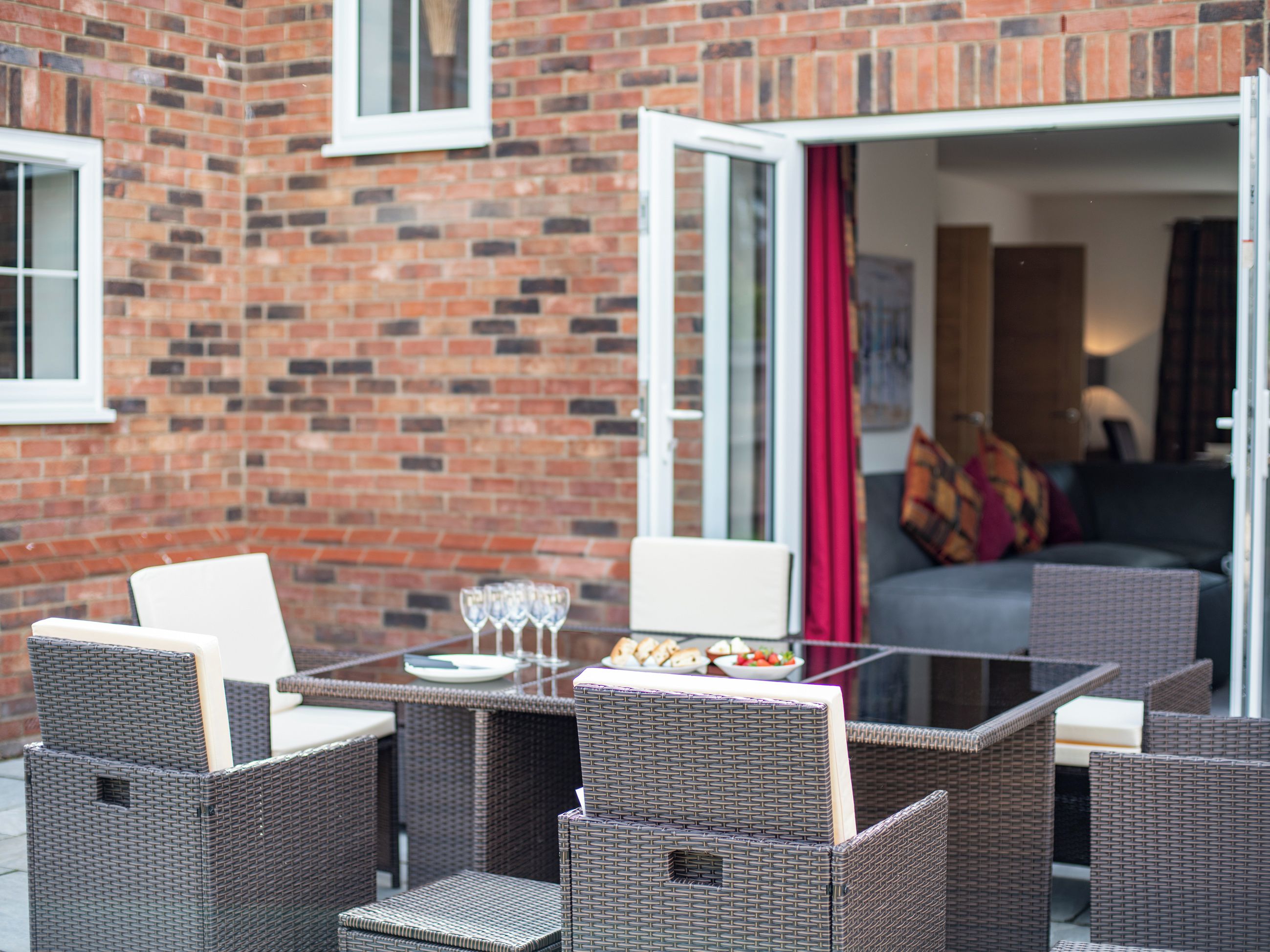 Un patio con mobiliario de mimbre, una mesa de vidrio y un muro de ladrillo.
