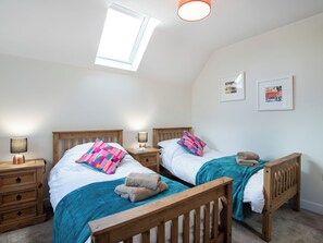 Une chambre à coucher avec deux lits en bois, une lucarne, des lampes de chevet et deux tableaux encadrés accrochés au mur.