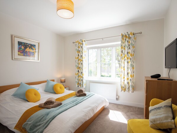 A bedroom with a bed, a bedside table, a lamp, a TV, and a window with curtains.