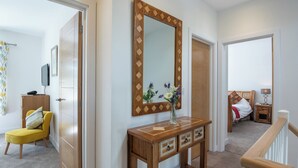 A hallway with a wooden console table, a mirror, a yellow chair, and a bed in the background.