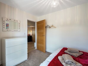 Quarto com cama, penteadeira, espelho e porta que dá para outro cômodo.