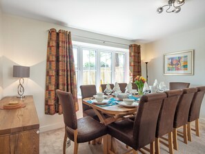 A dining area with a round table, brown chairs, a lamp, and a window with curtains. - 5 bedroom accommodation in Everton (Everton)