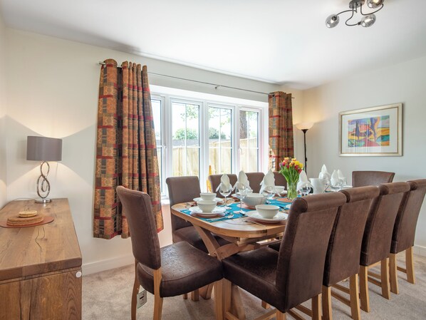 A dining area with a round table, brown chairs, a lamp, and a window with curtains.