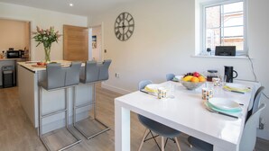 A modern kitchen with a dining area, a clock, and a window with a view.
